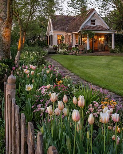 Charmante maison entourée de tulipes et autres fleurs printanières.