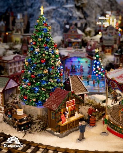Scène miniature de Noël avec un grand sapin illuminé et un marché.