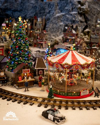 Village miniature de Noël avec manège et sapins illuminés.