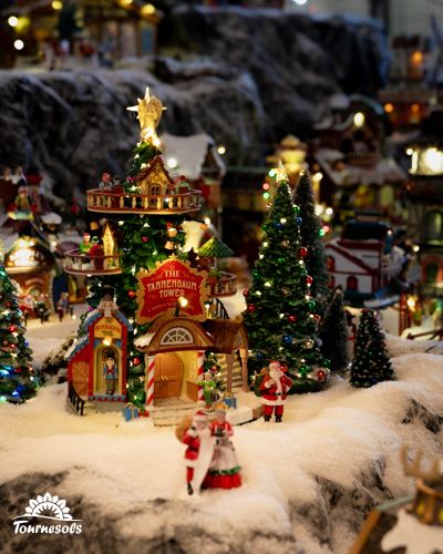 Village miniature de Noël avec sapins et maisons éclairées en décoration festive.