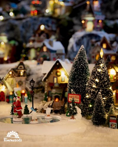 Village miniature de Noël avec décorations lumineuses et sapins enneigés.
