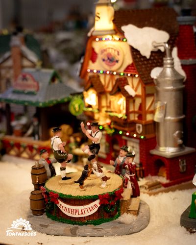 Scène festive de village miniature avec danseurs bavarois devant une maison illuminée.