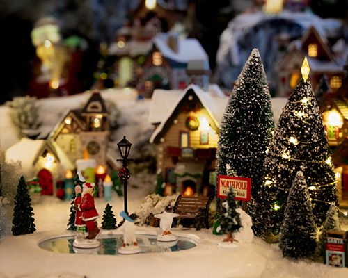 Village miniature de Noël avec figurines, sapins enneigés et maisons illuminées.
