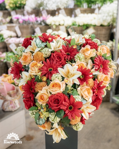 Composition florale en forme de cœur en roses rouges et pêche, gerberas et lis, exposée en jardinerie pour la Toussaint