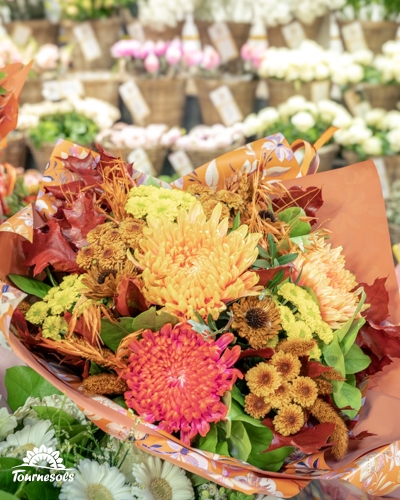 Bouquet automnal de chrysanthèmes orange et rose avec feuilles rousses, emballé de papier orange, en jardinerie Tournesols
