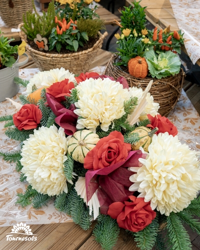 Composition de Toussaint aux chrysanthèmes blancs, roses rouges, mini-courges et branches de sapin, posée sur une table en