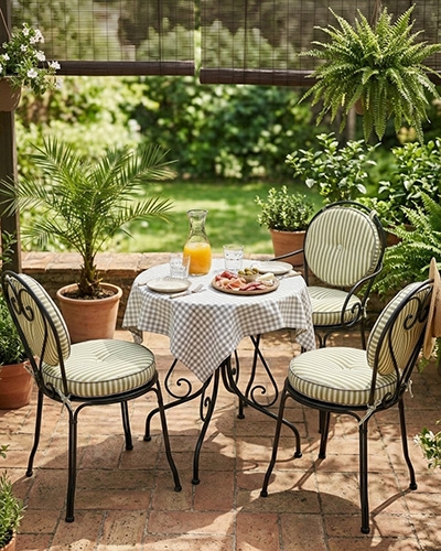 Salon de jardin en fer forgé avec table et chaises, coussins ronds rayés vert et blanc, sur une terrasse pavée.