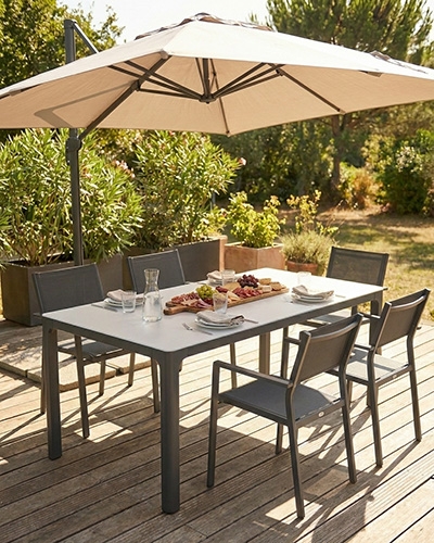 Table de jardin rectangulaire en bois et métal avec chaises assorties sur une terrasse pavée devant une maison en pierre.