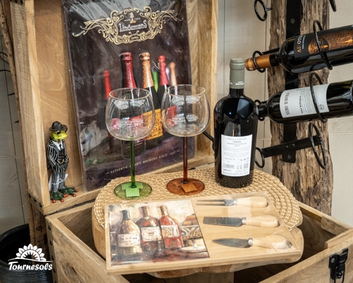 Coffret cadeau fête des pères : vin, verres à pied, planche et couteaux à fromage dans un décor rustique.